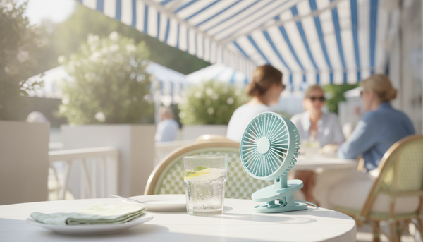 Petit ventilateur à pince bleu fixé sur une table de terrasse de café ombragée